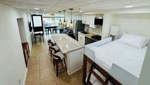 A compact hotel room with a kitchenette, a dining area, and a bed.