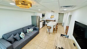 A modern living room with a grey sofa, a wooden dining table, and a TV.