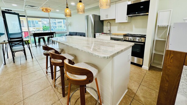 A modern kitchen with a central island, bar stools, stainless steel appliances, and pendant lighting.