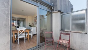 A modern patio with a sliding glass door leading to an interior dining area, a small seating area with two chairs, and a large window with a metal screen.