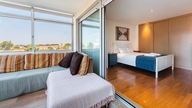 A modern bedroom with a large window, a bed, a sofa, and a small table.