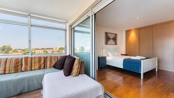 Un dormitorio moderno con un ventanal grande, una cama, un sofá y una mesita.