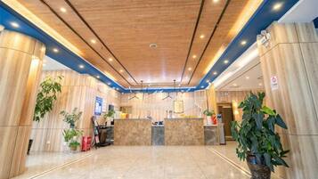 Un vestíbulo de hotel con mostrador de recepción, plantas en macetas y techo de madera.