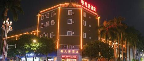 A multi-story hotel with illuminated signage, a ground-level restaurant, and a parking area with cars.