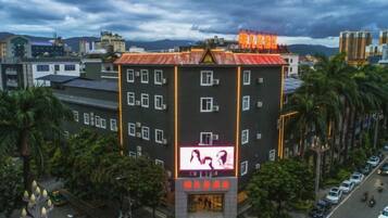 Um edifício de vários andares com um letreiro grande na fachada, cercado por carros estacionados e palmeiras.