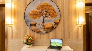 Un comptoir d’accueil avec un ordinateur portable, un tableau représentant un arbre et deux lampes fixées au mur.