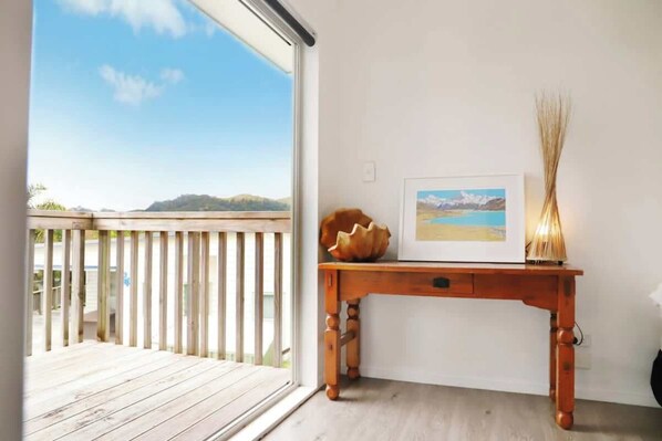 Une pièce dotée d’une terrasse en bois, d’un tableau encadré posé sur une table en bois, et d’un vase contenant des roseaux séchés.