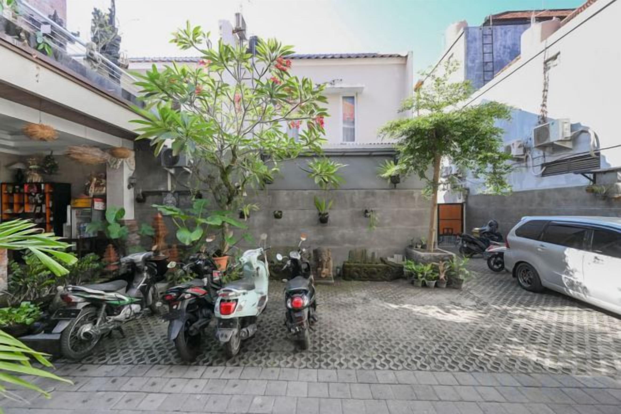 A courtyard with potted plants, a scooter, and a car parked on a patterned pavement.