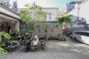 A courtyard with potted plants, a scooter, and a car parked on a patterned pavement. - RedDoorz near Mertasari Beach 2 (Bali)