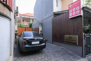 Ein schwarzes Auto steht in einer schmalen Gasse mit einem Holzzaun und einem Schild mit der Aufschrift 'RedDoorz'.