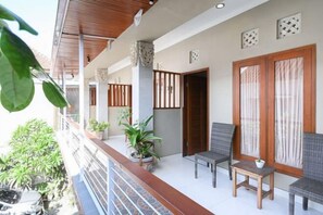 A balcony with potted plants, wicker furniture, and a wooden door. - RedDoorz near Mertasari Beach 2 (Bali)