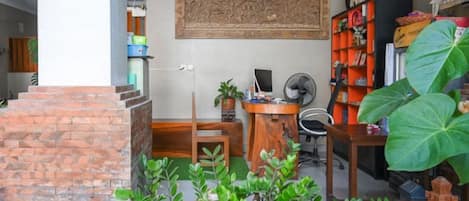 A room with a brick fireplace, a desk with a computer, a bookshelf, and a large plant.