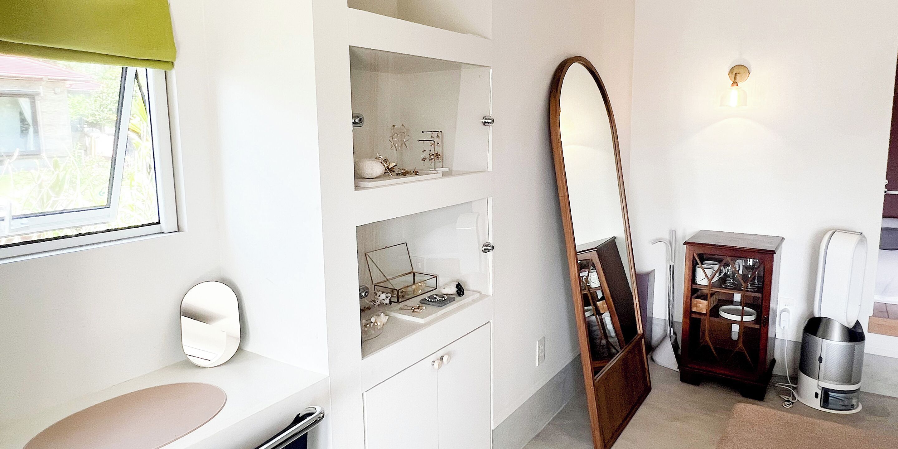 A modern bathroom with a large mirror, a sink, and a cabinet with decorative items.