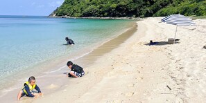 A beach with clear water, a sandy shore, and a striped umbrella. - HOLLY CAMP CASA (Amami)