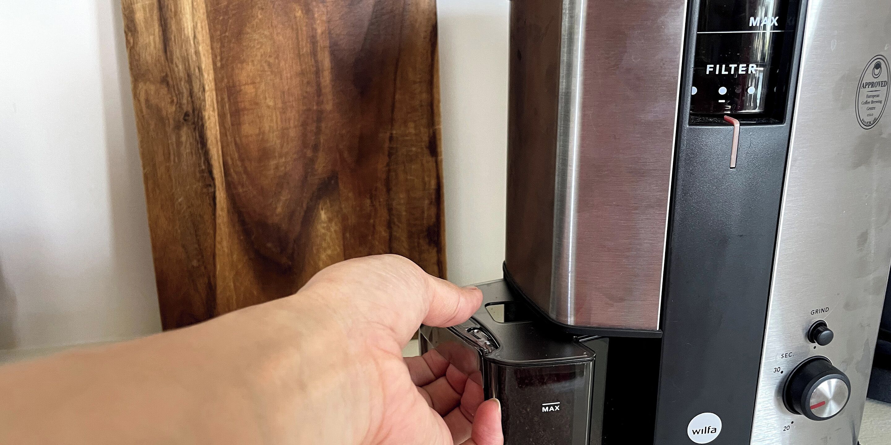 A hand adjusting a coffee machine with a filter compartment and a grind control knob.