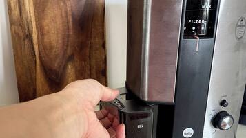 A hand adjusting a coffee machine with a filter compartment and a grind control knob.