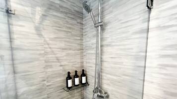A shower with a handheld showerhead and a wall-mounted faucet. There are three bottles on a shelf below the shower.
