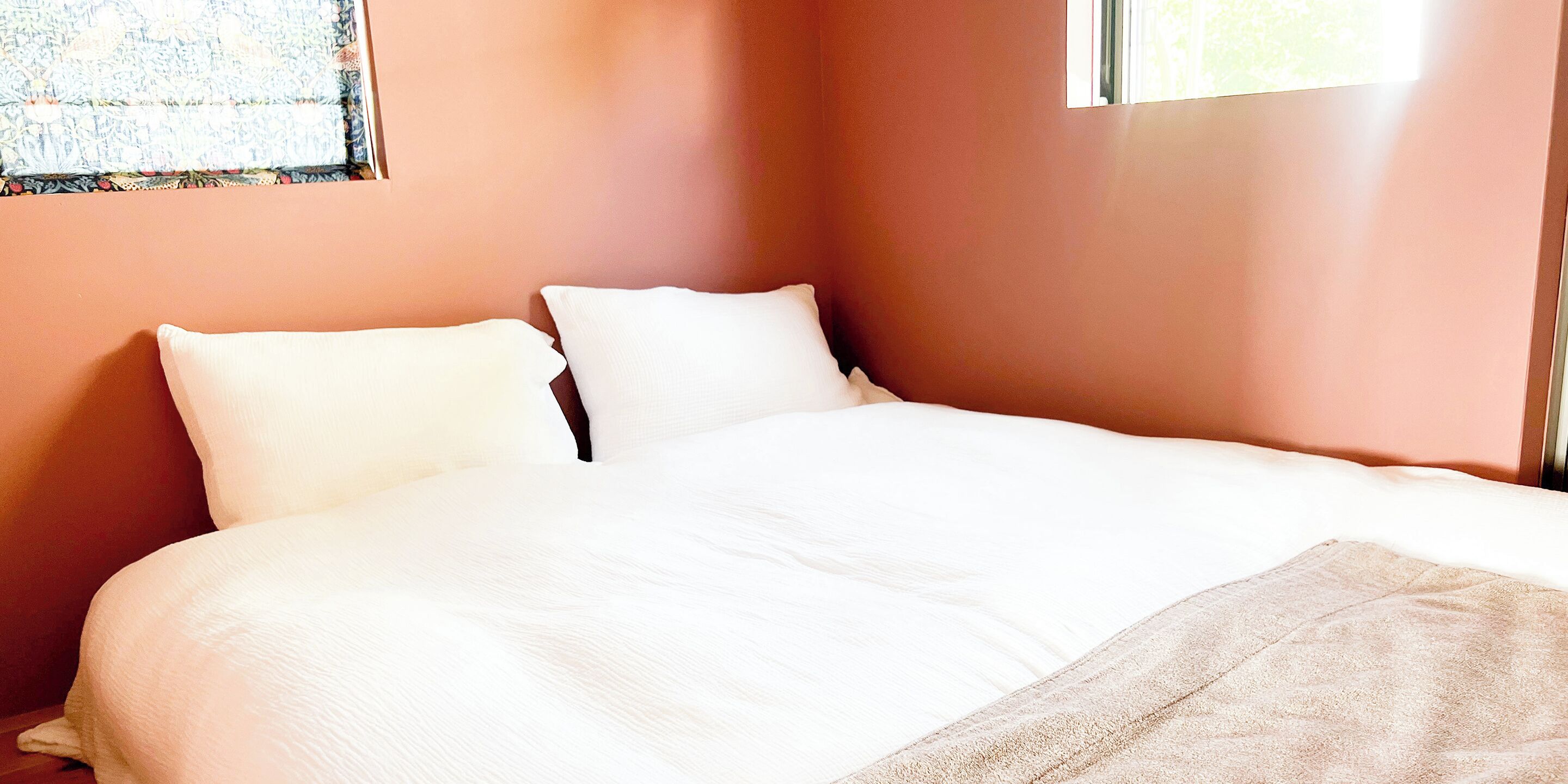 A neatly made bed with white linens and pillows in a room with peach-colored walls.