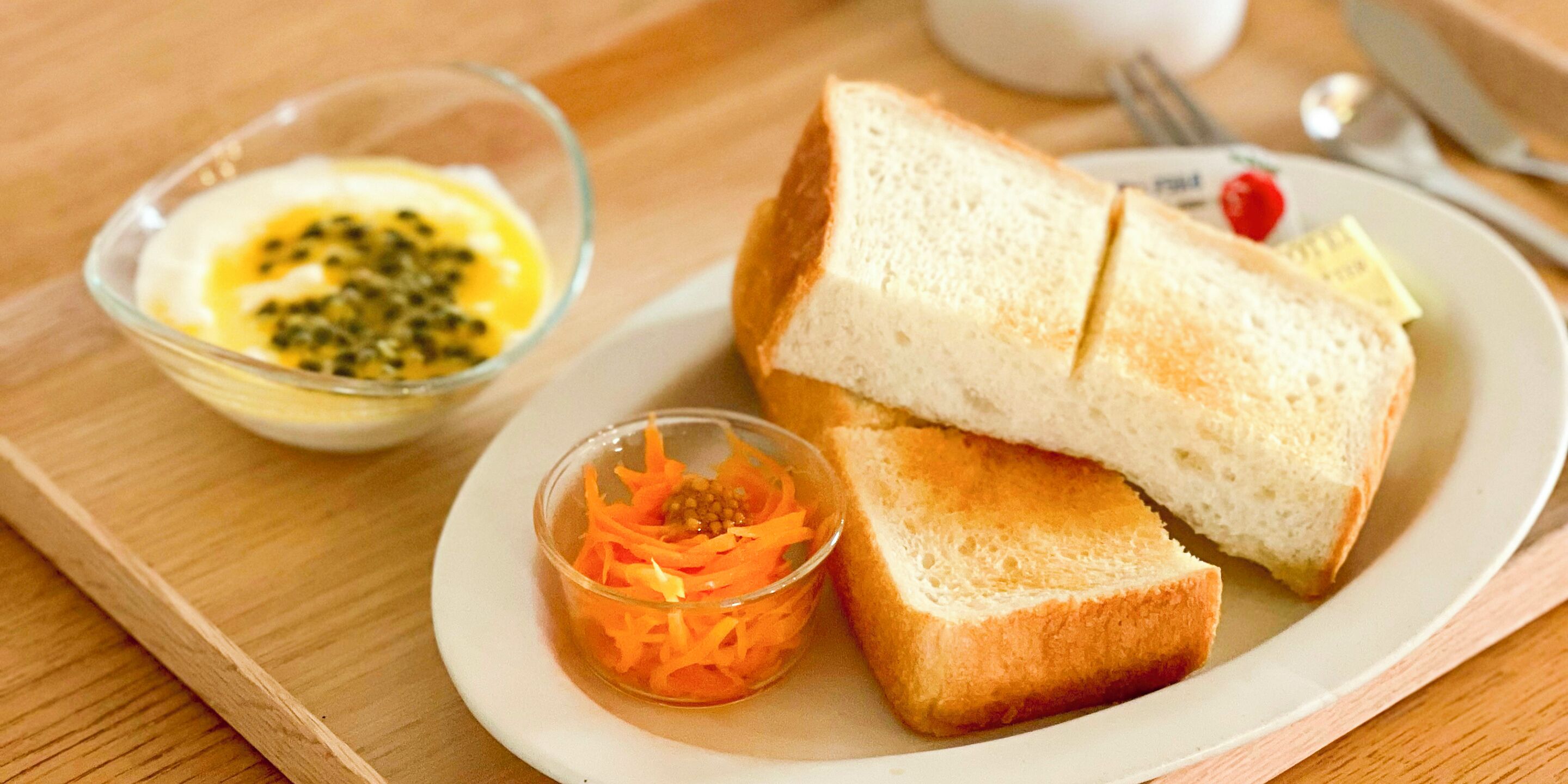 A plate with slices of white bread, a small bowl of carrot shreds, and a bowl of sauce with seeds.