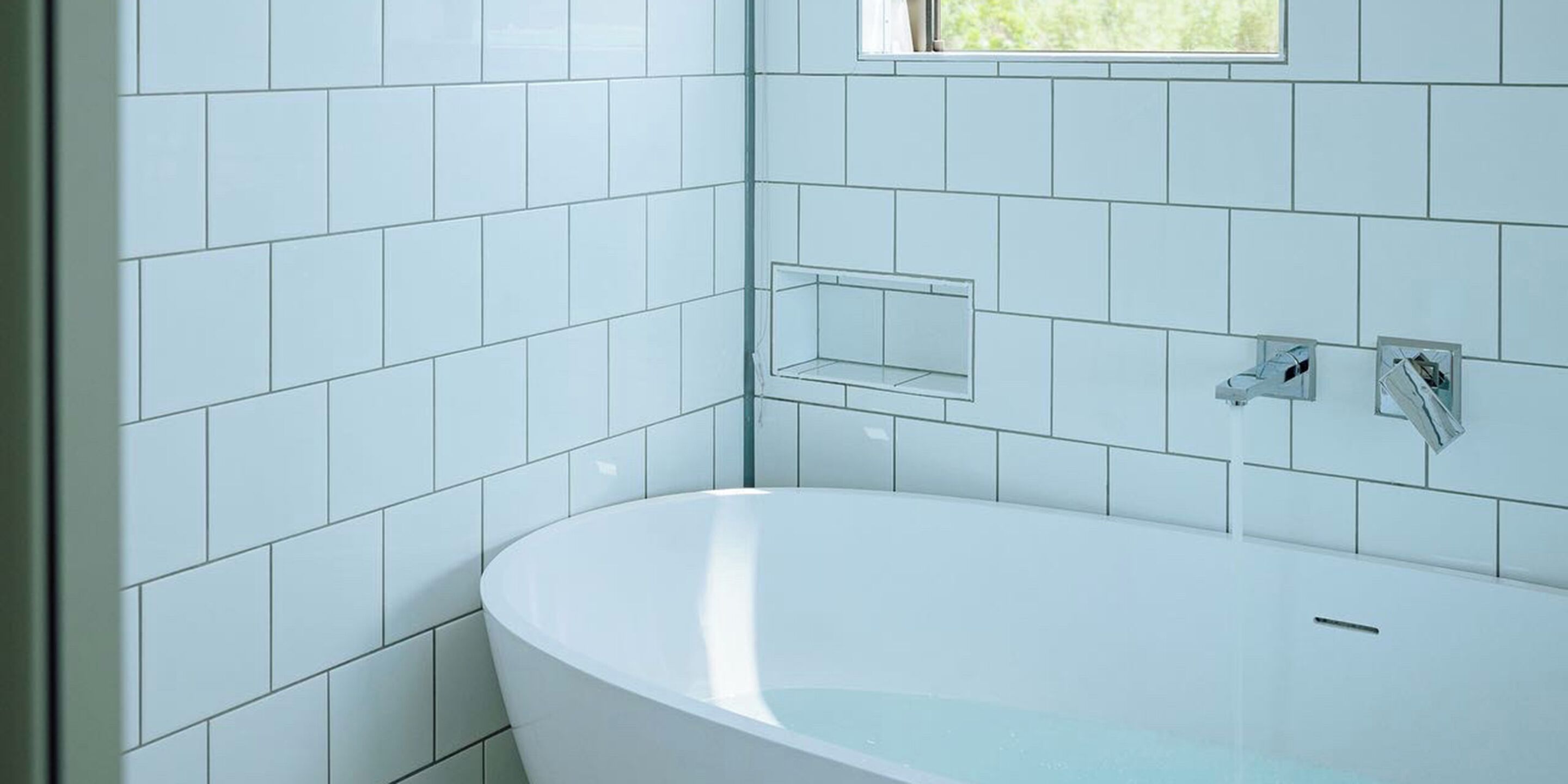Un baño moderno con azulejos blancos, una bañera independiente y un ventanal que proporciona luz natural.