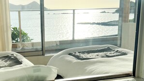 A hotel room with two beds, a large window offering a view of the sea and distant mountains. - HOLLY CAMP CASA (Amami)