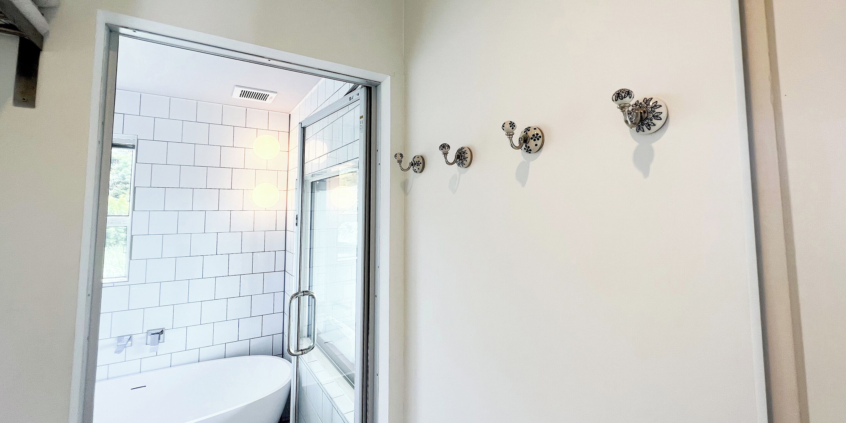 Un bany amb un lavabo blanc, una porta de dutxa de vidre i penjadors decoratius a la paret.