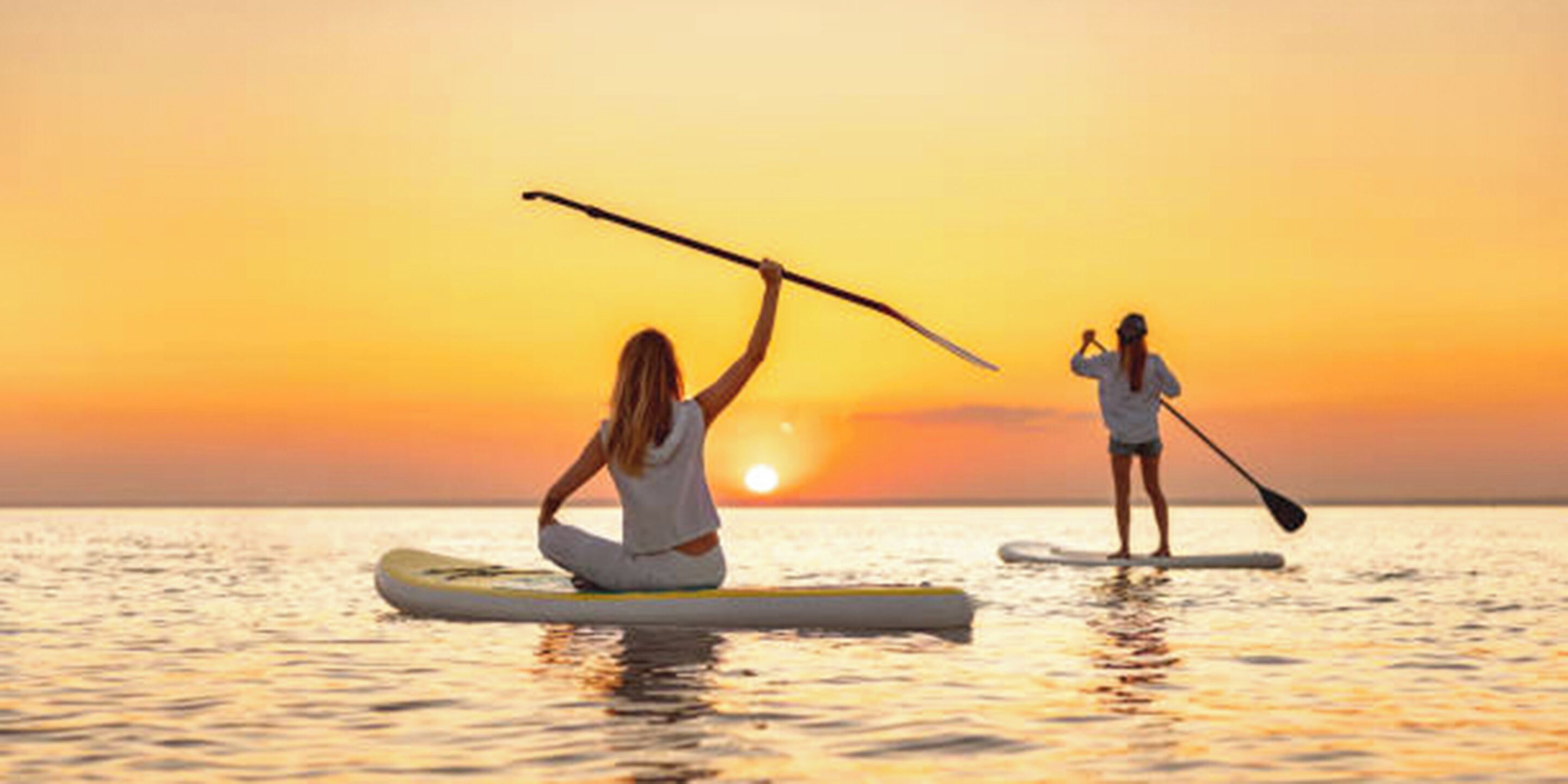Dos personas haciendo paddleboard en un mar tranquilo al atardecer.