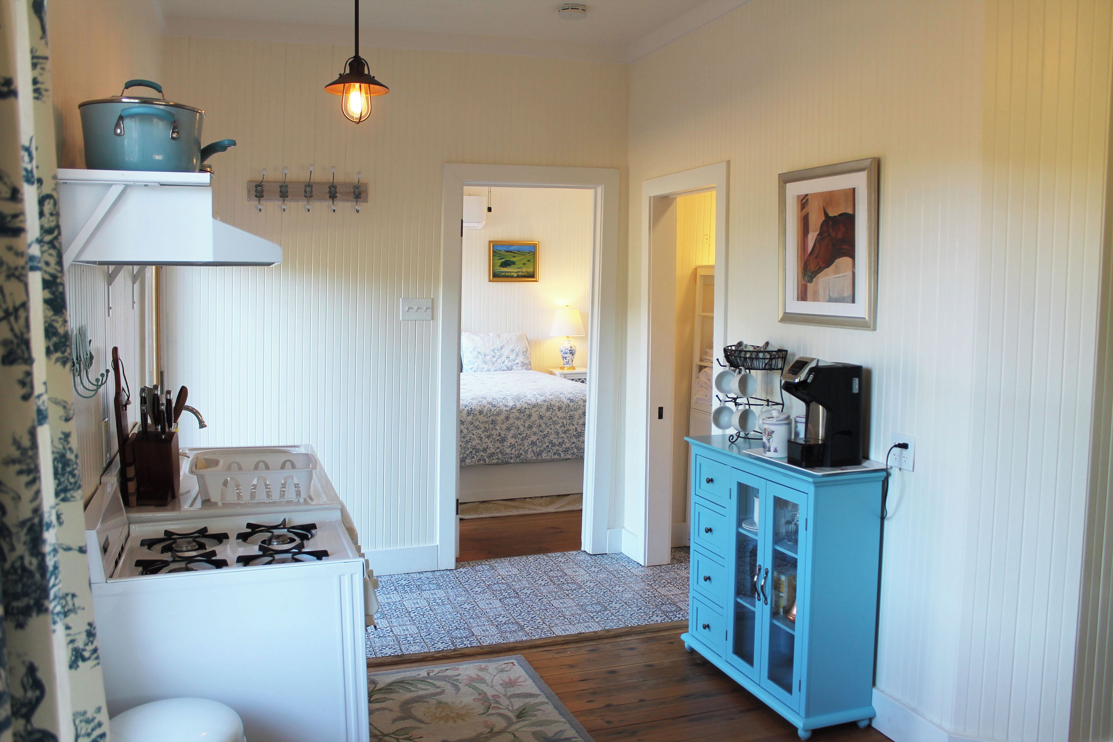 A compact kitchen with a gas stove, a blue cabinet with glass doors, and a hanging light fixture.