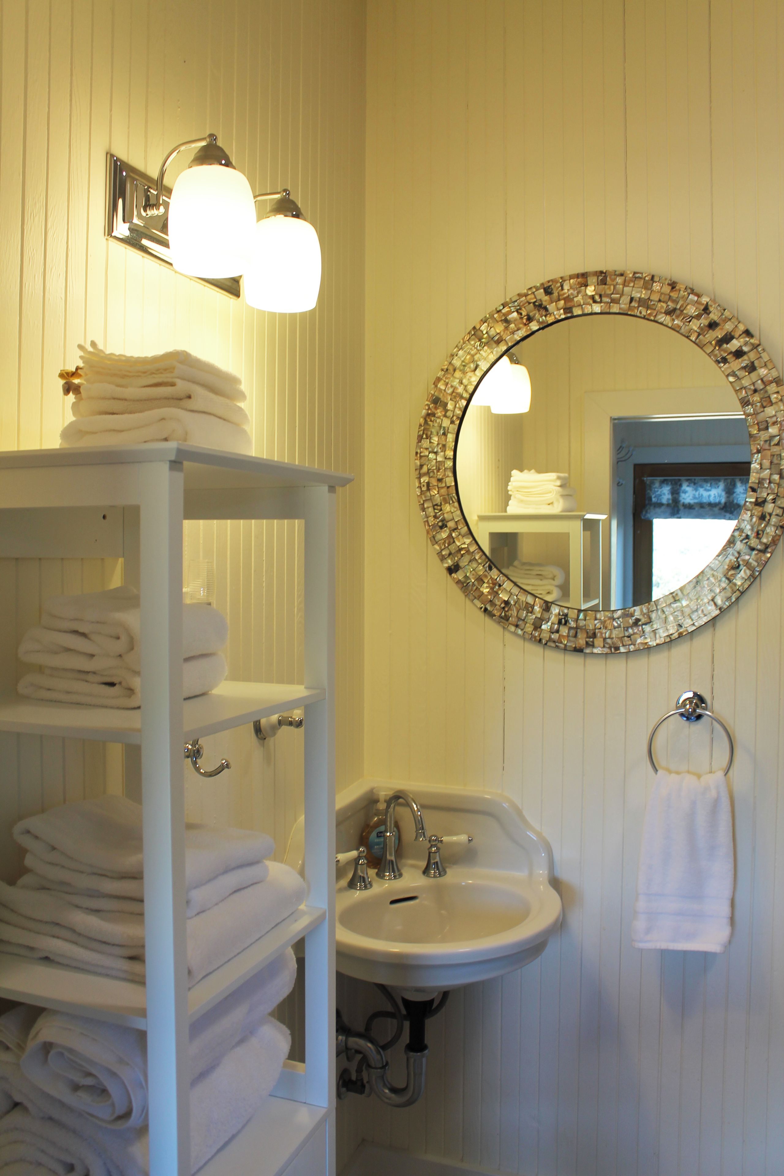 Une salle de bain avec un meuble-lavabo blanc, un évier et un miroir orné d’un cadre en mosaïque.