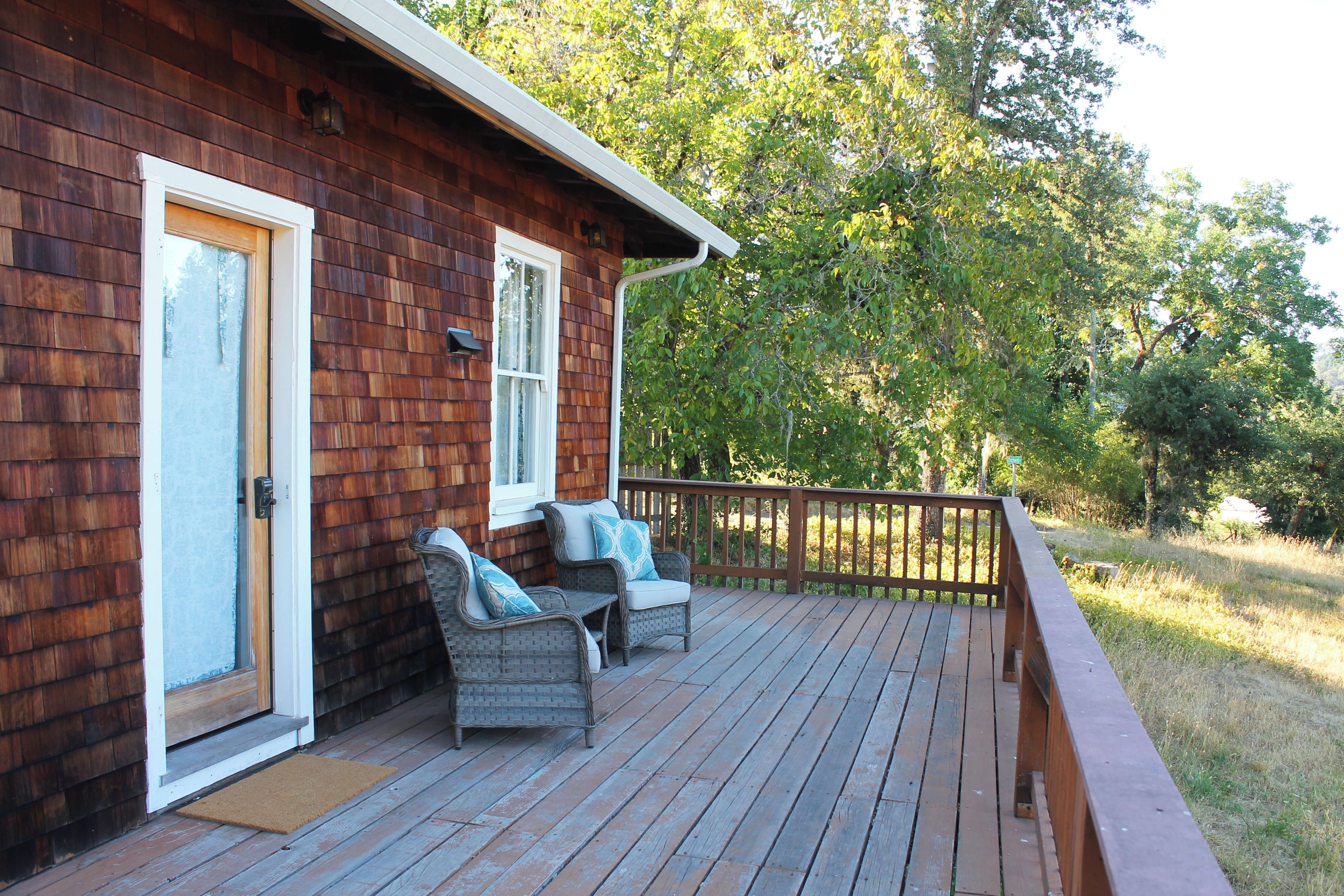 Eine Holzhütte mit Veranda, zwei Korbstühle mit Kissen und einer Holzterrasse.