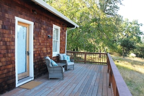 A wooden cabin with a porch, two wicker chairs with cushions, and a wooden deck. - Historic Cottage at Ridgewood Ranch, Home of Seabiscuit (Willits)