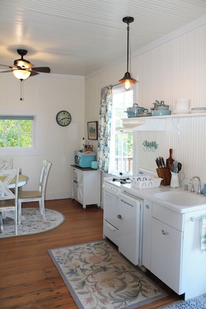 A kitchen with white cabinetry, a stove, a sink, and a ceiling fan. - Historic Cottage at Ridgewood Ranch, Home of Seabiscuit (Willits)