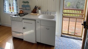 A kitchen with a gas stove, sink, and white cabinets. There is a window with curtains and a view of trees outside. - Historic Cottage at Ridgewood Ranch, Home of Seabiscuit (Willits)