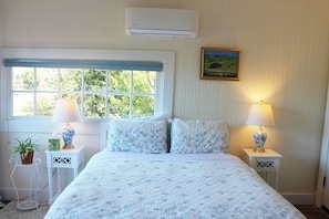 A bedroom with a large window, two bedside lamps, a painting on the wall, and a potted plant. - Historic Cottage at Ridgewood Ranch, Home of Seabiscuit (Willits)