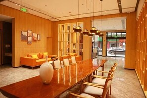 A hotel lobby with a long wooden reception desk, comfortable seating, a large vase, and a view of the street through glass doors. - Aegean • Cultural Tourism Hotel (Zitong)