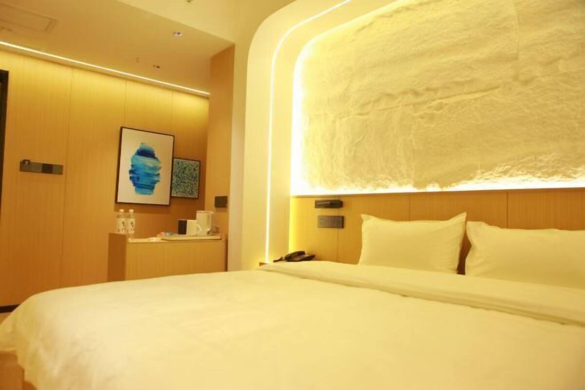 Quarto de hotel com uma cama grande, uma mesinha de cabeceira com telefone e luminária na parede.