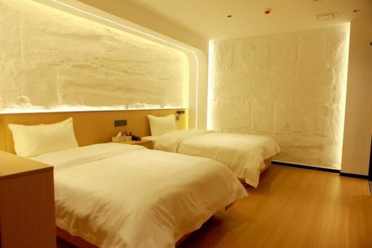 Quarto de hotel com duas camas, piso de madeira e parede texturizada.