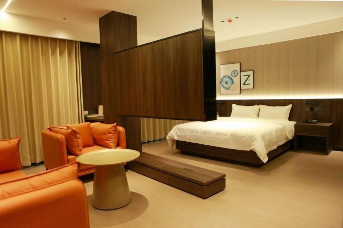 Quarto de hotel moderno com cama, sofá laranja e uma pequena mesa.