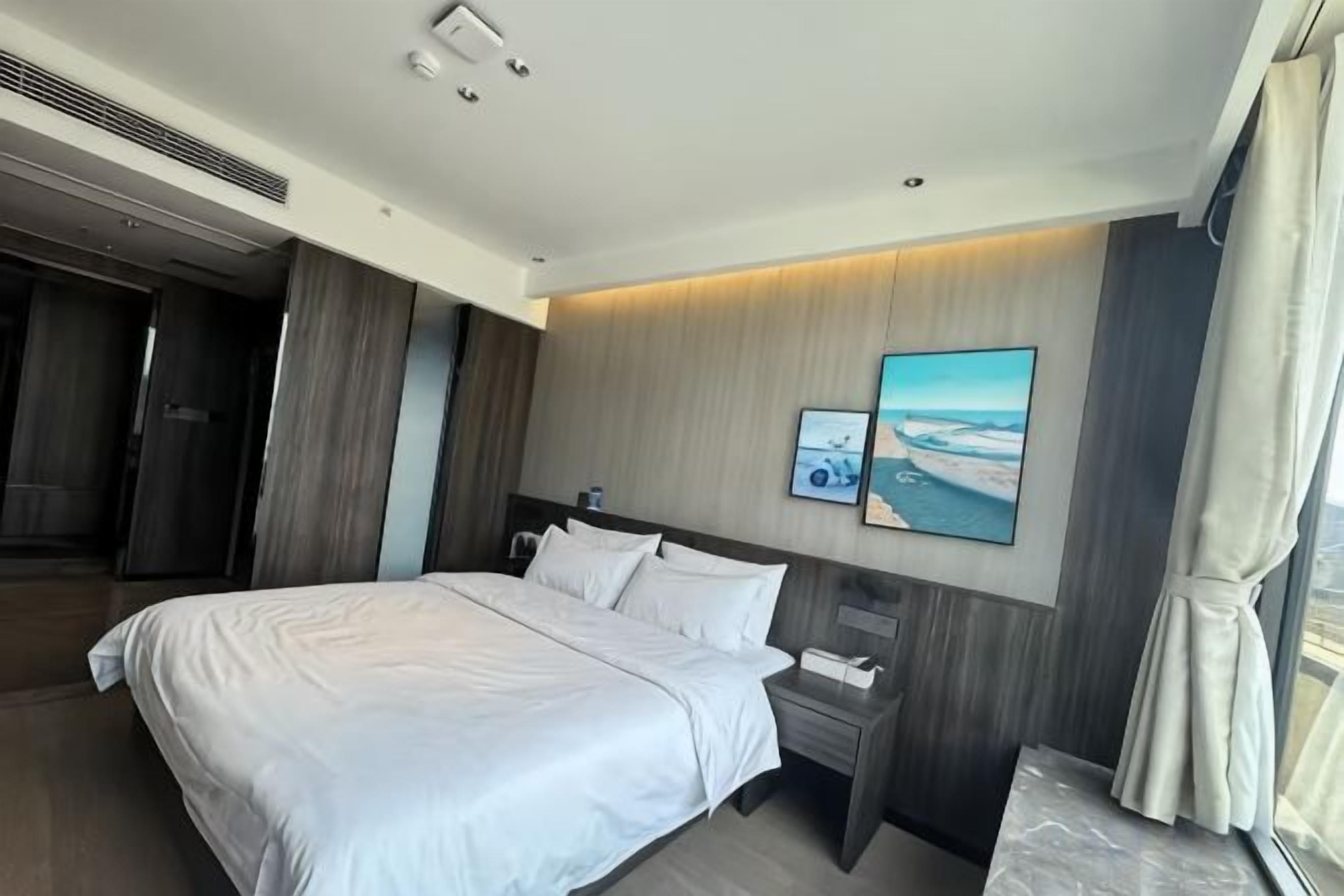 A modern hotel room with a large bed, a bedside table, a nightstand, and a wall-mounted TV.