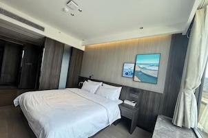 A modern hotel room with a large bed, a bedside table, a nightstand, and a wall-mounted TV.