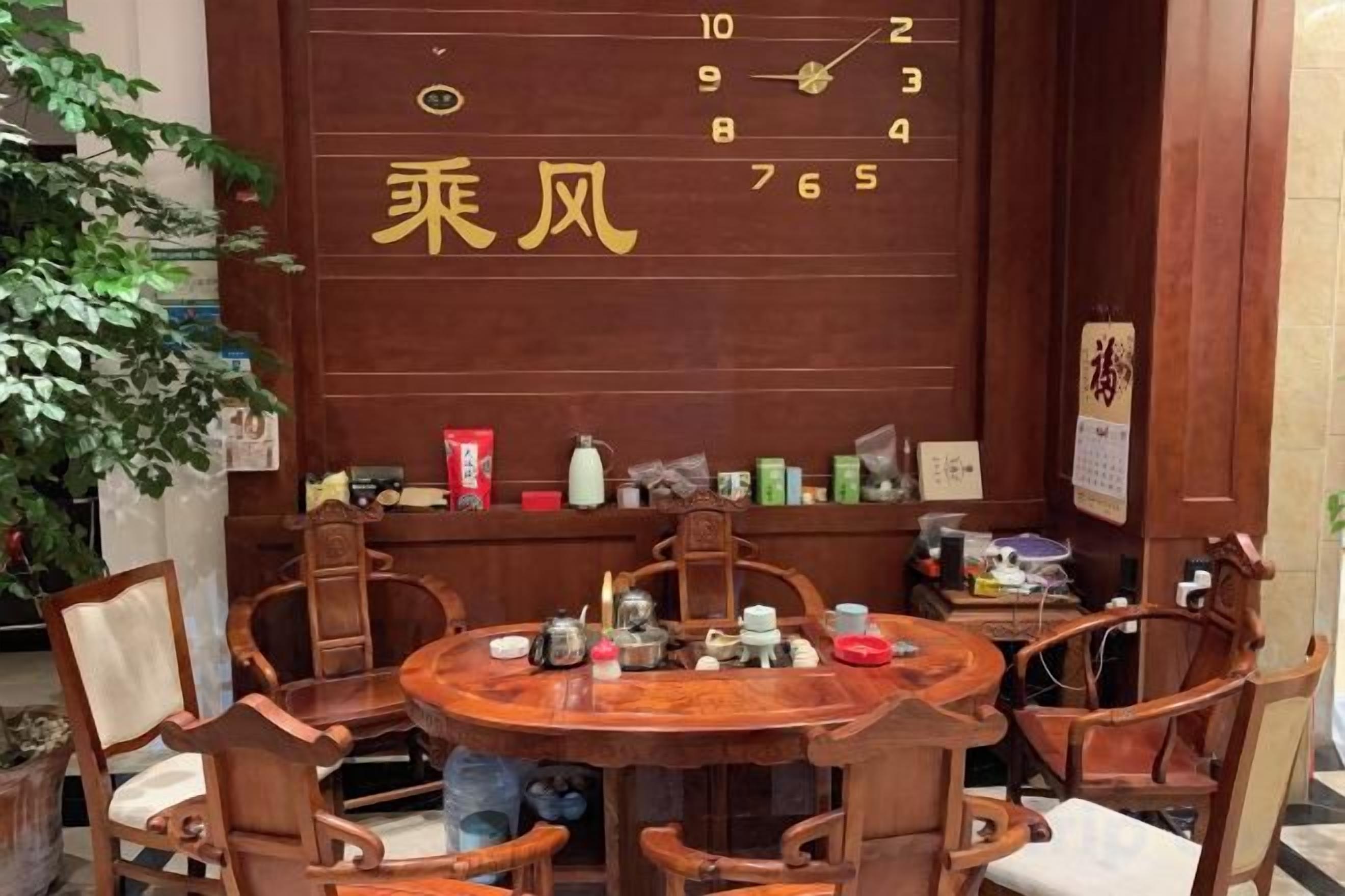 A traditional wooden dining table with chairs, a wall with a calendar, and various items on shelves.