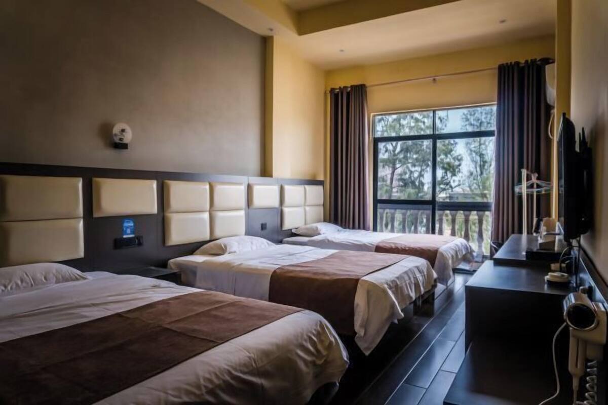 Ein Hotelzimmer mit zwei Betten, einem Schreibtisch, einem Fernseher und einem Fenster mit Vorhängen.