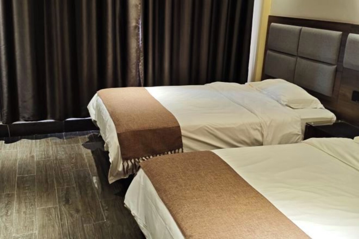A hotel room with two beds, a dark curtain backdrop, and a wooden floor.