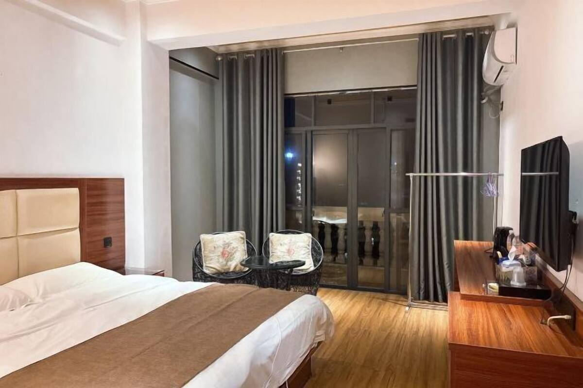 Ein Hotelzimmer mit Bett, kleinem Tisch, zwei Stühlen, Schreibtisch und einer Glastür, die auf einen Balkon führt.
