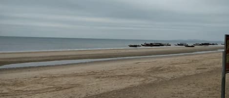 A beach with a sandy shore and a calm sea. Boats are anchored in the water.