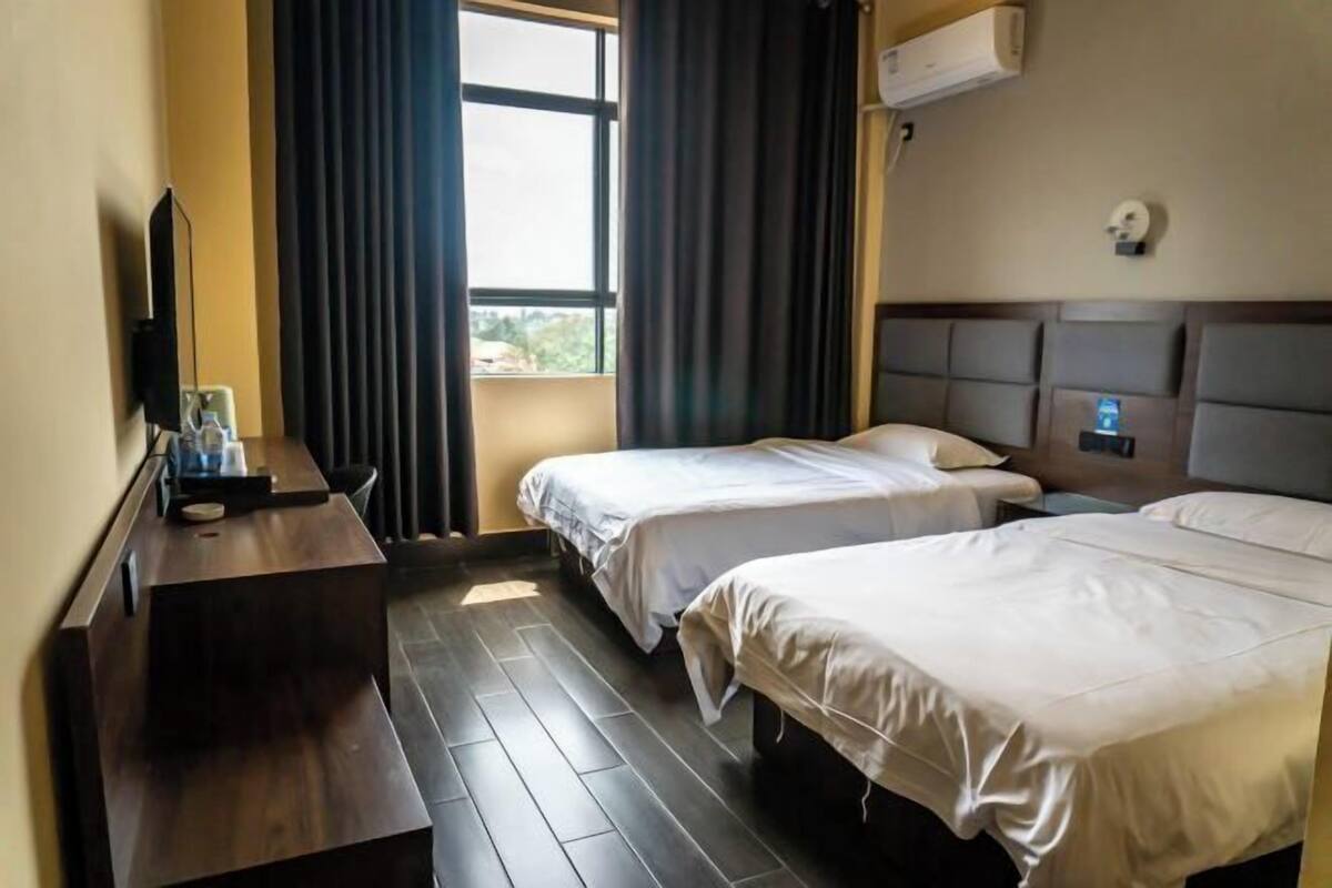 Ein Hotelzimmer mit zwei Betten, einem Schreibtisch mit Computer und einem Fenster mit Vorhängen.