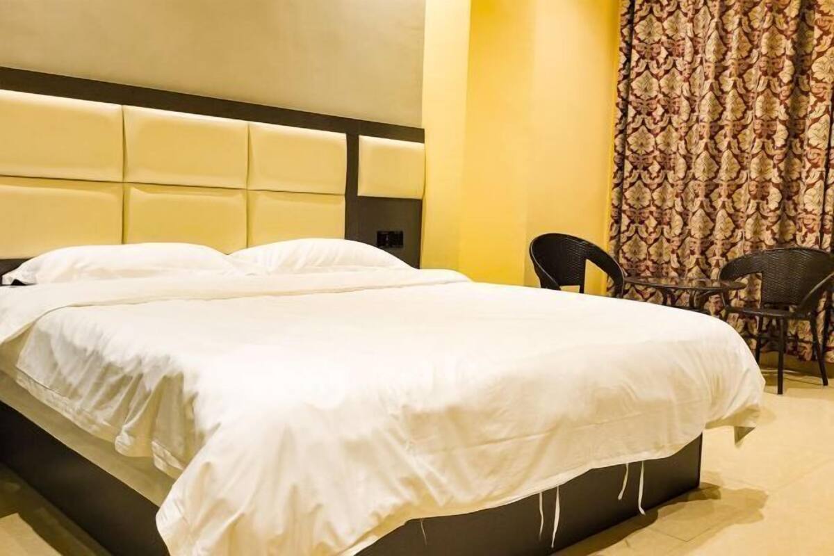 Ein Hotelzimmer mit einem großen Bett, einer gepolsterten Kopfteil, einem Sessel und einem gemusterten Vorhang.