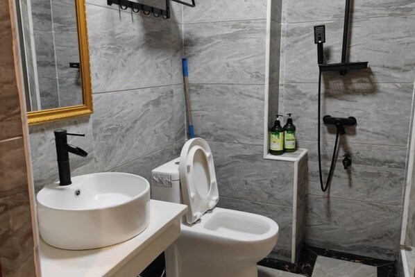 Een badkamer met een wit wastafel, toilet en douche. Er staan flessen shampoo en conditioner aan de muur.