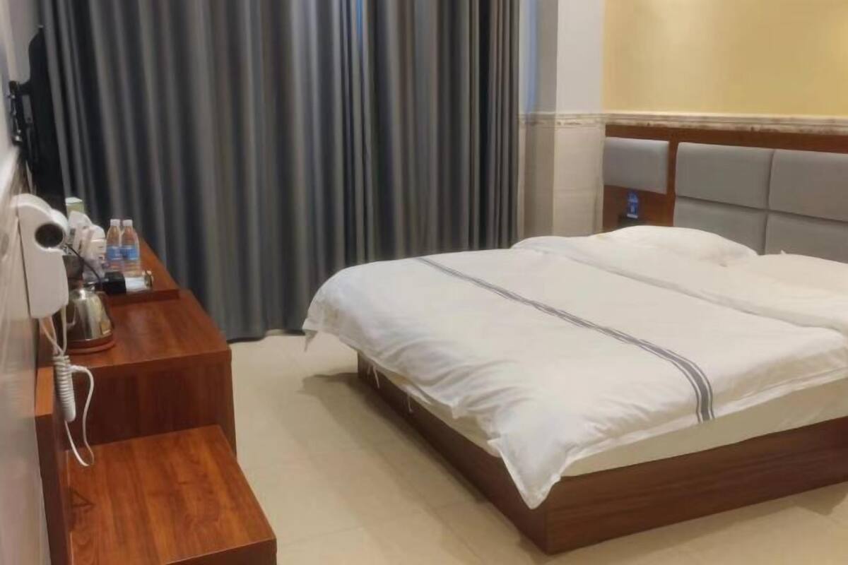 Ein Hotelzimmer mit einem Bett, einem Nachttisch aus Holz mit einer Lampe und einem Vorhang.