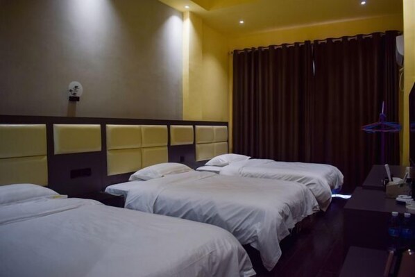 A hotel room with three single beds, a desk with a chair, and a large window with curtains.